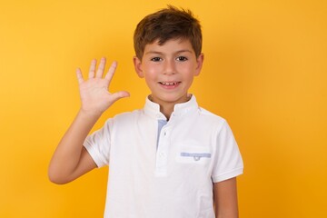 little cute Caucasian boy kid wearing white t-shirt against yellow wall showing and pointing up...