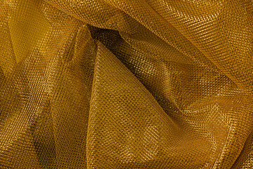The texture of a thin nylon transparent fabric close-up in Fortuna Gold color. Pattern, background in color trend 2021