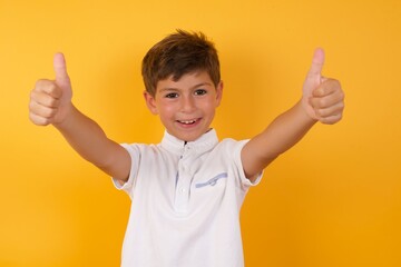 Amazed little cute Caucasian boy kid wearing white t-shirt against yellow wall points down with...