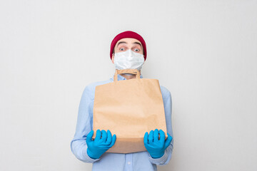 Fototapeta na wymiar It is difficult for a courier with a medical mask and medical gloves to hold a paper bag. Concept of safe delivery. Portrait, mockup