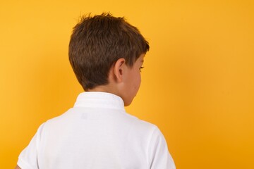The back view of little cute boy kid wearing white t-shirt against yellow wall Studio Shoot.