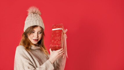 Dreaming winter girl holding christmas present on red background