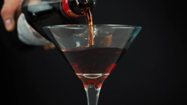 man pours martini into glass on black background