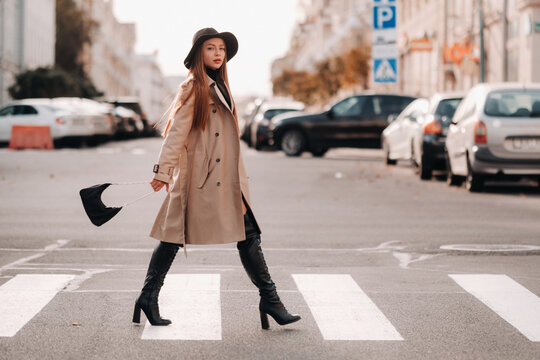 Stylish young woman in a beige coat in a black hat on a city street. Women's street fashion. Autumn clothing.Urban style