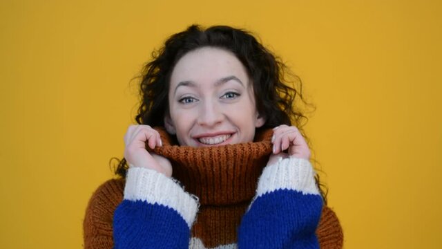 Beautiful brunette girl portrait with curly hair in a knitted winter sweater on a yellow background