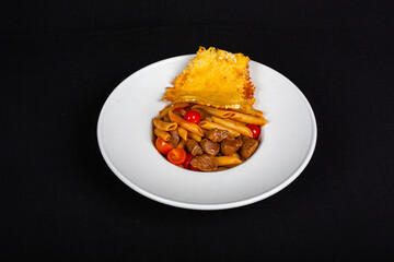 Pieces of meat with pasta on plate and black background