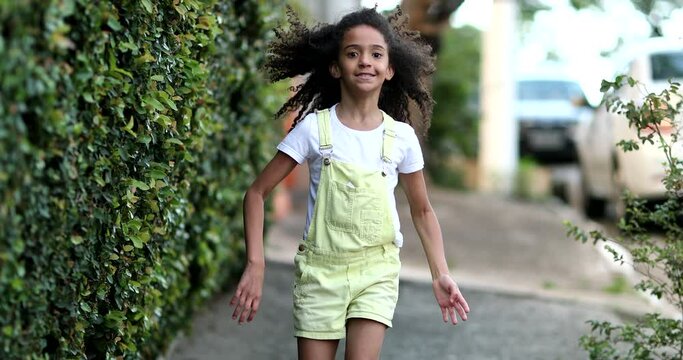 Happy little girl hopping outside in city sidewalk. Mixed race kid walking and jumping outdoors. Child skipping outdoors