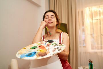 Artist woman posing in front of the canvas with her palette. Painting artist posing on chair at sunset.