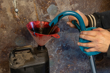 Waste oil from a car engine is pumped into an oil tank for disposal.