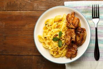 A plate of pasta in a creamy sauce with cheese and chicken on a napkin next to a fork. copy space.