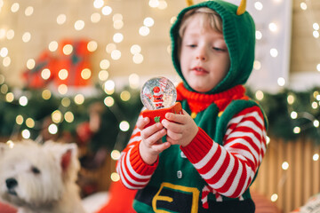 Happy new year concept. Happy blond child sits on the bed, opens a box and takes out a gift glass...