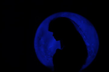 Fototapeta na wymiar A female doll silhouette in the night in front of a circular light source with space to write your text 
