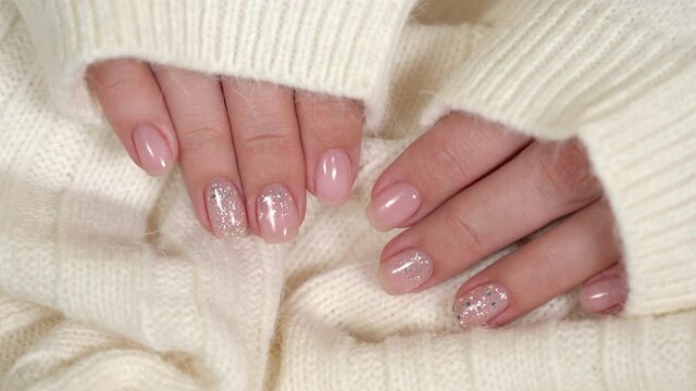 Closeup top view of beautiful faded pastel color trendy manicure of pink nails with glossy silver shiny design isolated on knitted white texture. Winter, autumn, spring style of naildesign concept.