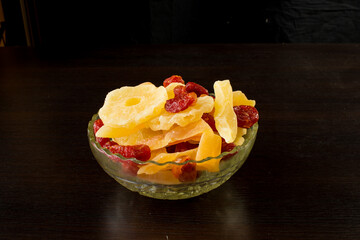 Yellow candied melon slices, pineapple rings and dogwood in a glass vase on a black background