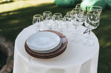 Empty glass wine glasses and plates stand on a round white table, covered with a tablecloth, as decorations for a banquet, buffet table.