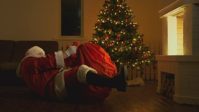 Santa Claus with bag of gifts crawls out of fireplace at Christmas or New Year.