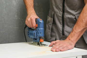 repairman's hand is sawing with electric jigsaw on the table