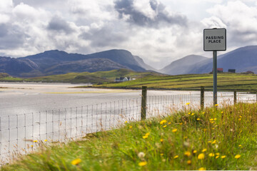 Beautiful Scottish scenery of Passing Place sign in front of Uig beach with hills and glens in the...