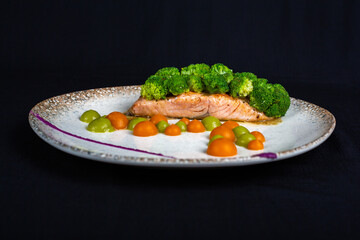 Tuna steak covered with broccoli and decorations on white plate and black background