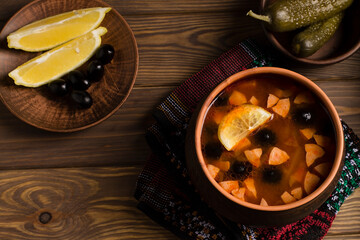 Solyanka soup with meat, sausage, vegetables, olives and lemon in a plate.