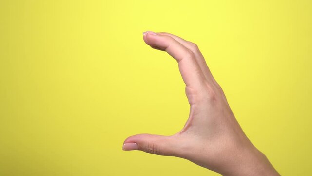 Empty female hand showing different sizes of virtual invisible objects from big to small. Hand isolated on yellow backgrond.