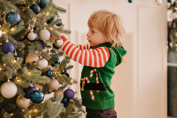 Cute little child decorates the Christmas tree with balls