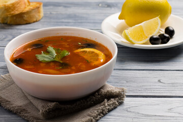Solyanka soup with meat, sausage, vegetables, olives and lemon in a plate.