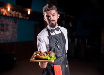 Young waiter helpfully serves dish on a black background.