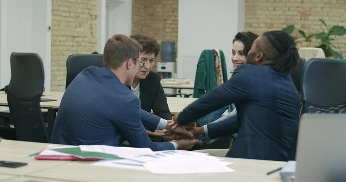 Wide shot of friendly multiethnic colleagues stacking hands in office. Handstack of happy confident men and women enjoying teamwork. Partnership concept. Cinema 4k ProRes HQ.