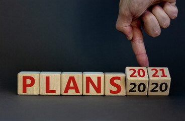 Business concept of planning 2021. Male hand flips wooden cubes and changes the inscription 'Plans 2020' to 'Plans 2021'. Beautiful grey background, copy space.