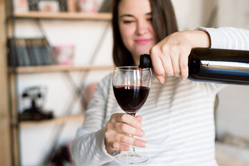 Pregnant alcoholic woman is pouring wine from a bottle into a glass and drinking.