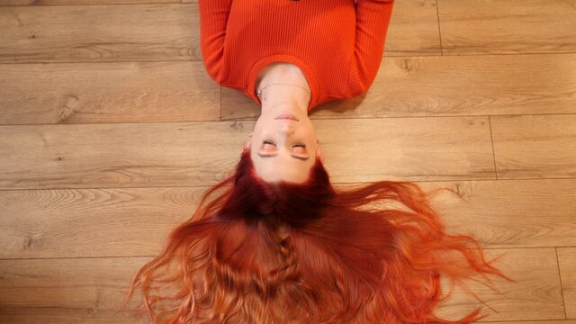 Redhead young pretty woman lie on a floor hair spreaded like a crown watch hold smartphone in social media