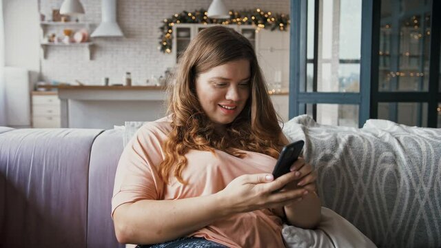 Millennial plus size lady spending time at home with smartphone, networking in social media, watching news online