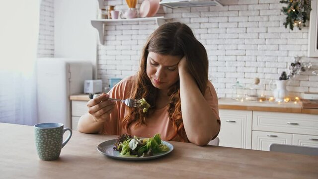 Boring diet. Depressed overweight woman eating untasty healthy salad at kitchen