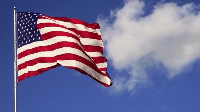 American flag waving against blue sky and white clouds.