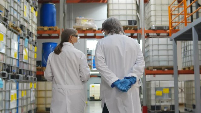 Back view of specialists in lab coat and gloves walking in industrial warehouse