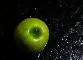 One green apple on wet black background