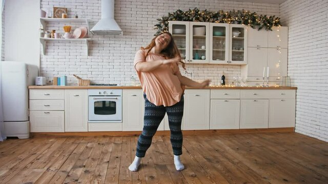 Body positive concept. Slow motion of happy overweight woman dancing at kitchen interior at home