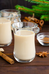 Hot tea with milk, cinnamon, cardamom, anise and other spices, Indian masala tea in a glass cup on a wooden background. Vertical, copy space.