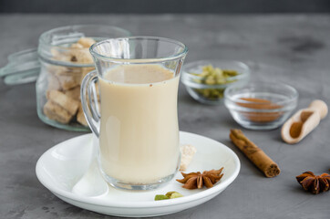 Obraz na płótnie Canvas Hot tea with milk, cinnamon, cardamom, anise and other spices, Indian masala tea in a glass on a dark background. copy space.