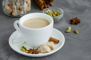 Hot tea with milk, cinnamon, cardamom, anise and other spices, Indian masala tea in a white cup on a dark background. copy space.