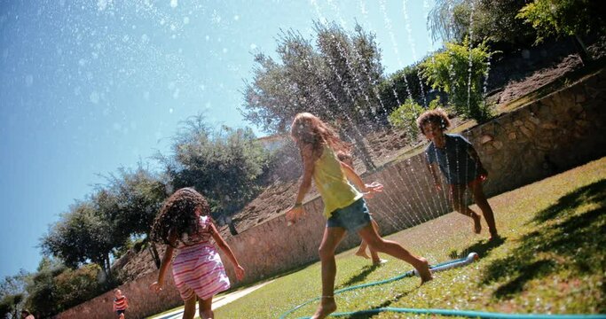 Kids playing and jumping over sprinkler on garden