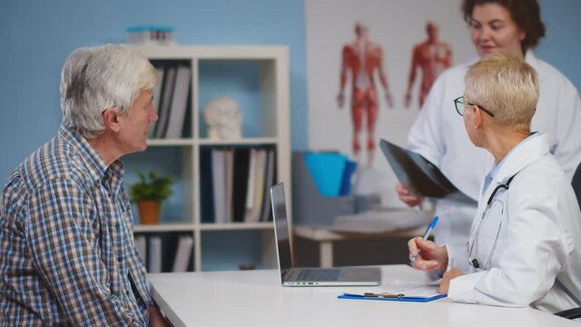 Physician talking and looking at x ray film with senior man at clinic