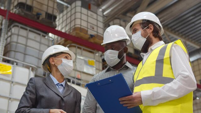 Diverse warehouse inspectors wearing safety mask discussing distribution plan on clipboard