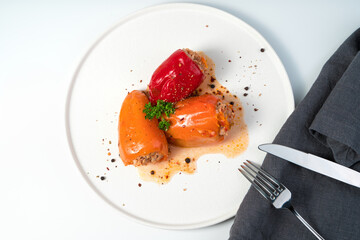Three stuffed peppers of orange and red color were sprinkled with spices and herbs in a white flat plate. The view from the top. The concept of healthy nutrition.