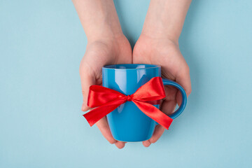 Pov top above overhead close up view photo of female hands holding bright color blue cup wrapped in red ribbon isolated over blue desk