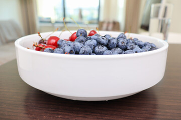 Raw juicy berries of sweet cherry and blueberry in a white ceramic dish