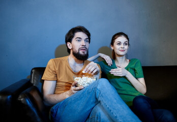 a man and a frightened woman watching a movie in the evening on the couch with a plate of popcor