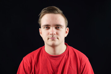 Young man in casual t-shirt standing against isolated dark background