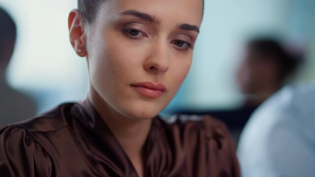 Pensive businesswoman sitting at workplace. Serious female worker looking away